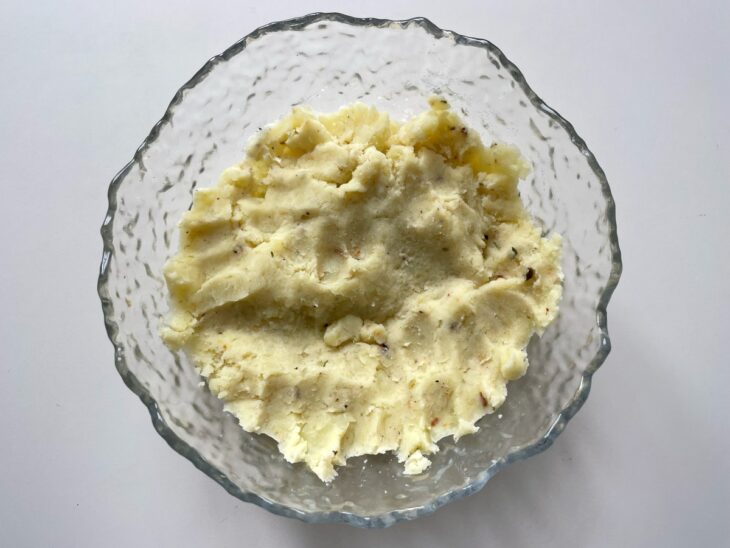 Batatas amassadas em uma tigela com farinha e noz-moscada.