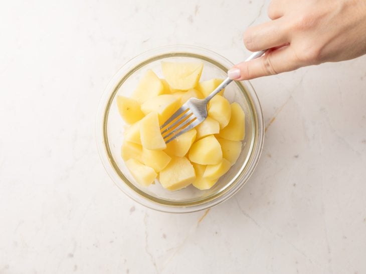 Batatas em um recipiente com um garfo para amassar.