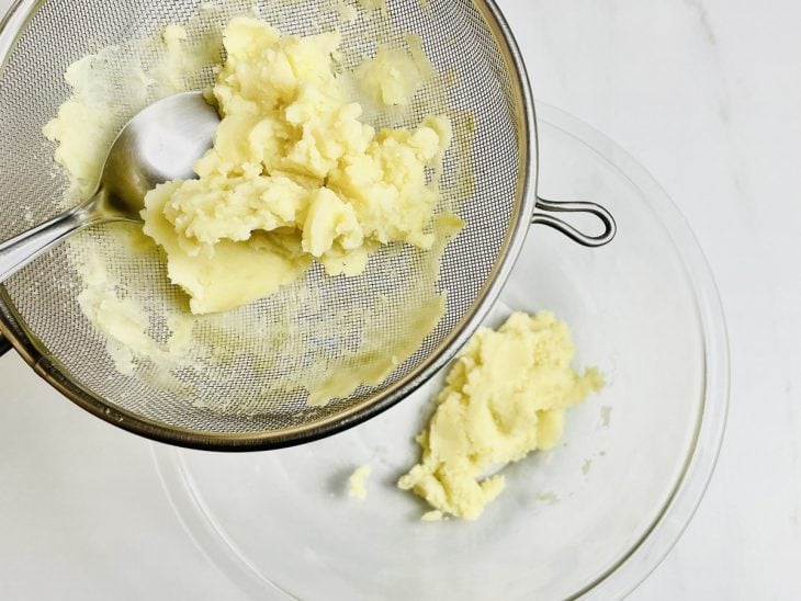 Purê de batatas sendo passado por uma peneira.
