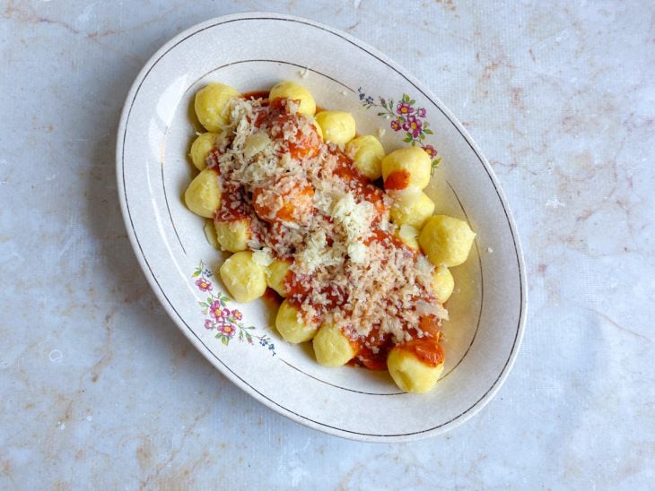 Molho de tomate e queijo parmesão ralado adicionados sobre as bolinhas de nhoque.