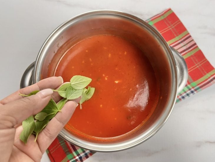 Uma panela com molho para nhoque e folhas de manjericão.