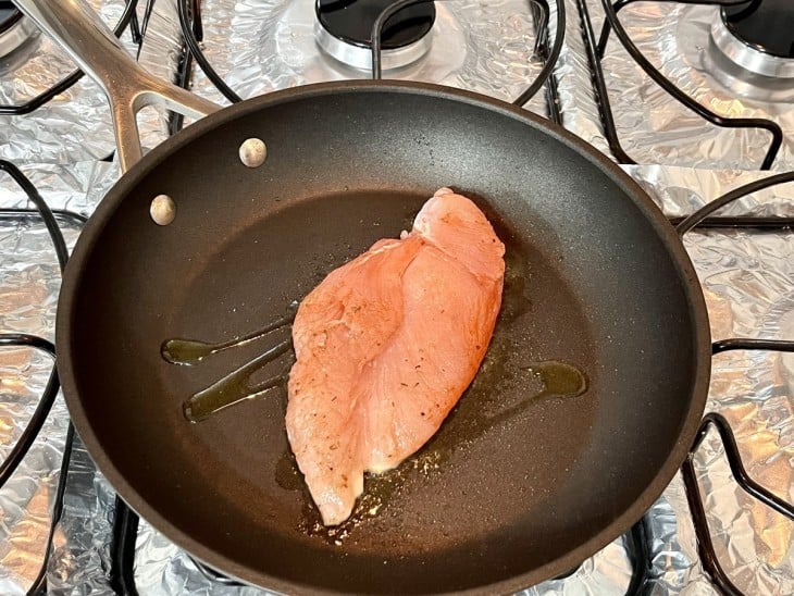 Filé de frango em uma frigideira preta com óleo.