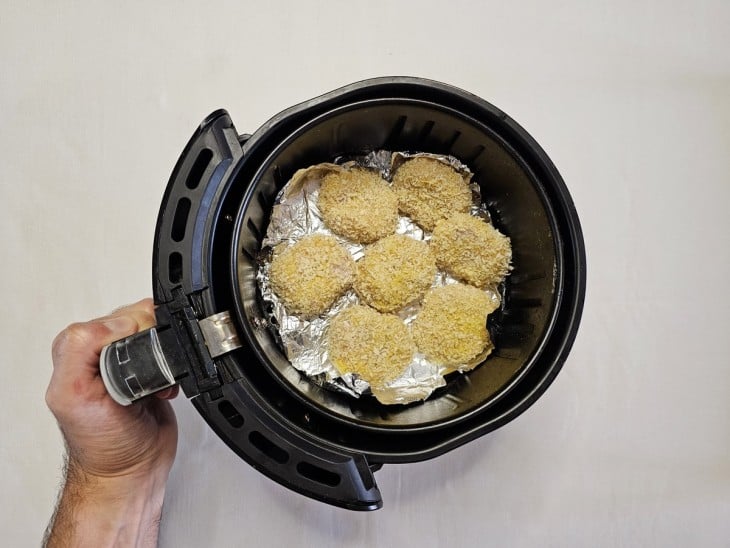 Uma cesta de air fryer forrada com papel alumínio e os nuggets crus.