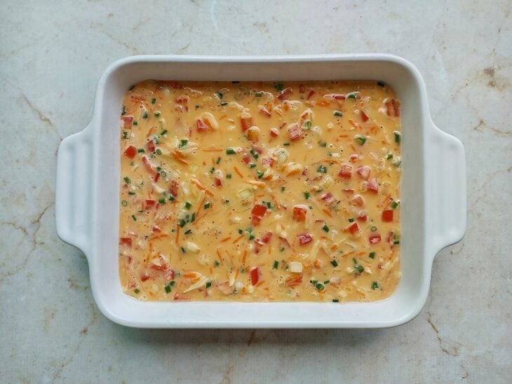 Mistura de ovos e legumes sendo vertida em um refratário retangular untado.