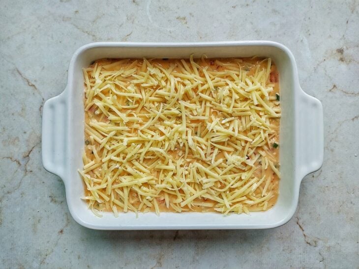 Queijo mussarela ralado sendo espalhado uniformemente cobrindo toda a superfície do omelete.