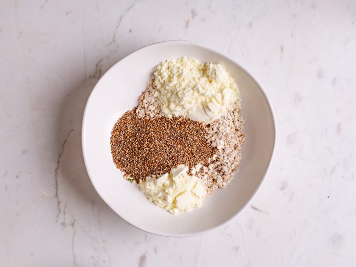 Aveia, chia, whey protein, leite em pó e água em uma tigela.