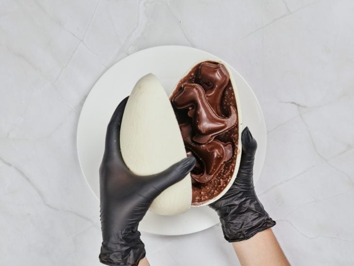 Metades do ovo de Páscoa sendo fechadas com os dinossauros de chocolate dentro.