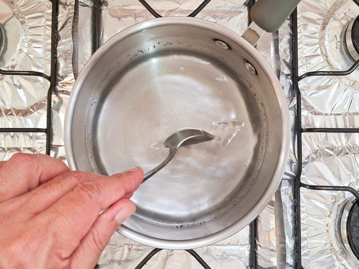 Água sendo mexida com uma colher na panela para formar um redemoinho.