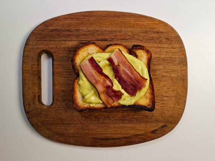 Creme de avocado e bacon acomodados sobre uma fatia de pão.