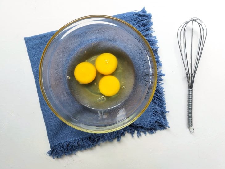 Ovos colocados em uma tigela e fouet ao lado.
