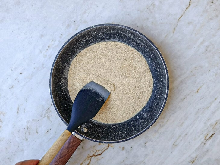Farinha de mandioca sendo tostada em frigideira enquanto é mexida constantemente.