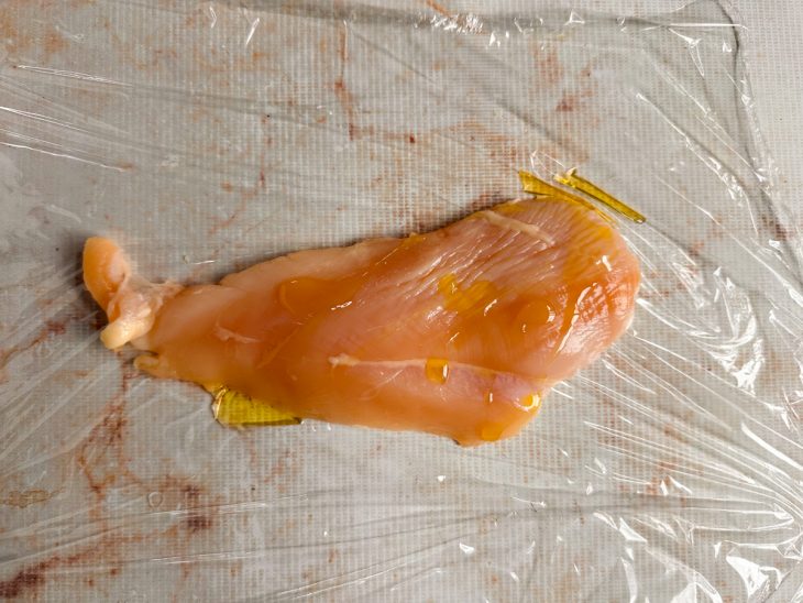 Filé de frango coberto com plástico e untado com azeite.