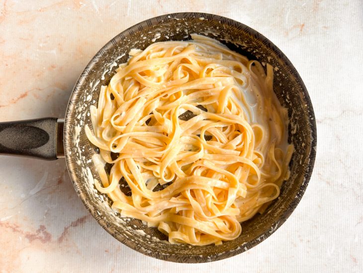 Fettuccine envolvido no molho cremoso de parmesão no fogo baixo.