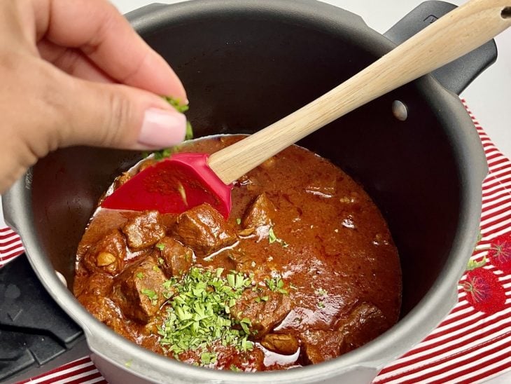 Uma panela de pressão contendo carne ao molho com temperos.