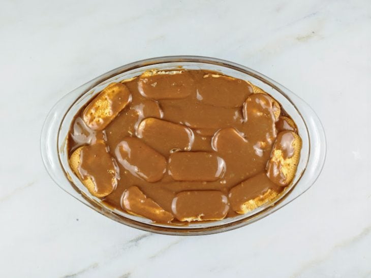 Camadas de bolachas e brigadeiro intercaladas na travessa.