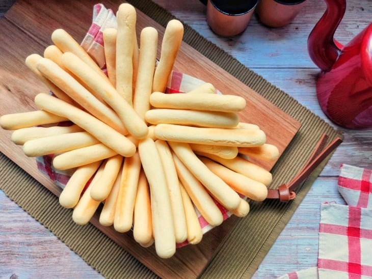 Um recipiente contendo vários palitos de queijo simples e crocantes.