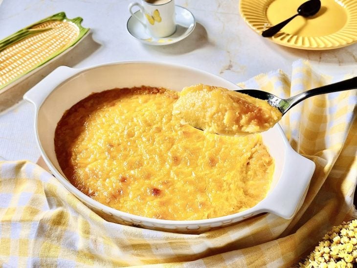 Pamonha de forno pronta para consumo em um refratário e uma porção em evidência em uma colher.