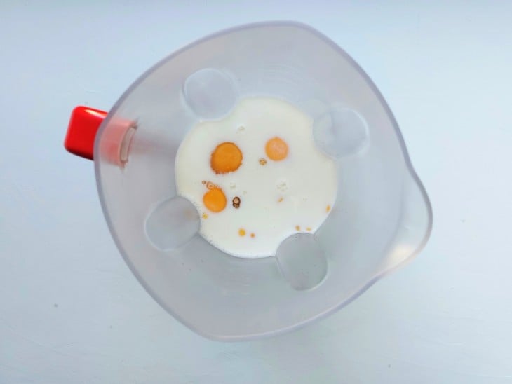 Ovos, leite e milho juntos no liquidificador de copo na cor transparente e alça na cor vermelha.