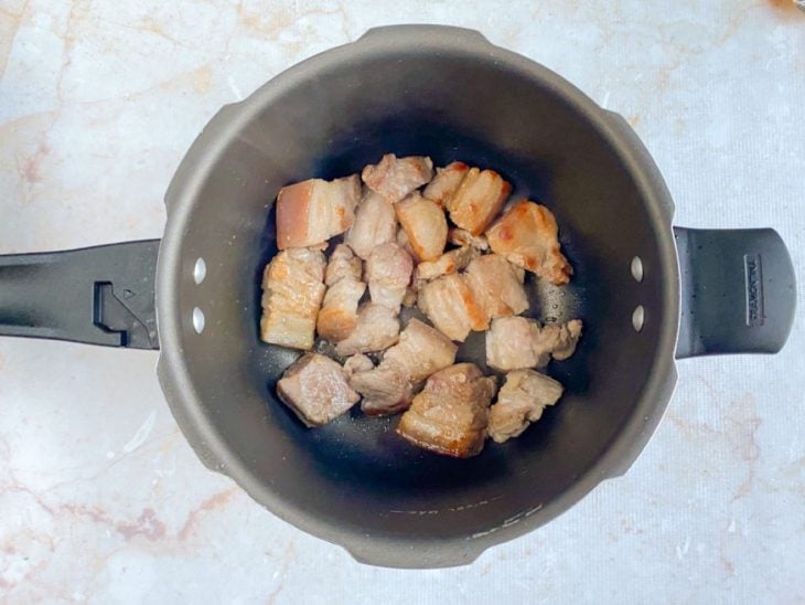Pedaços de panceta selados em uma panela com azeite.
