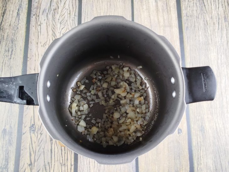 Alho e cebola refogados em óleo numa panela de pressão.