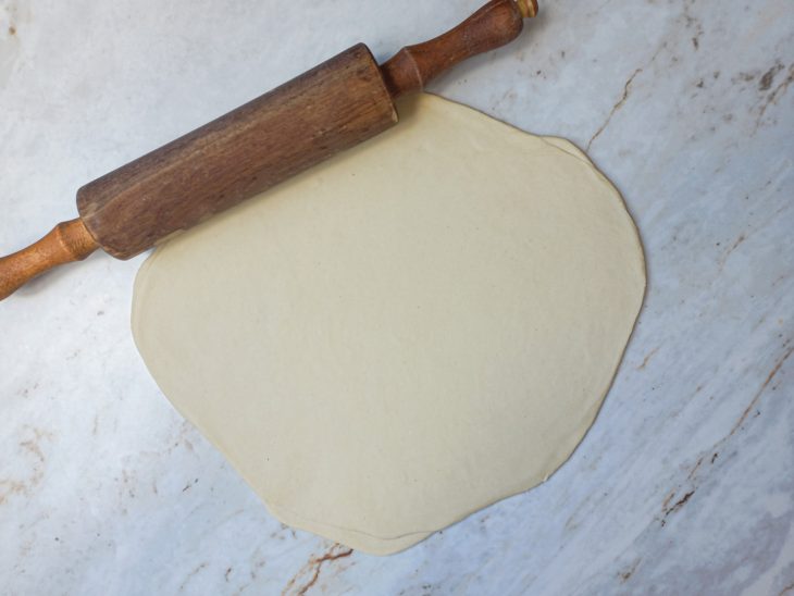 Na bancada, massa aberta em disco fino.