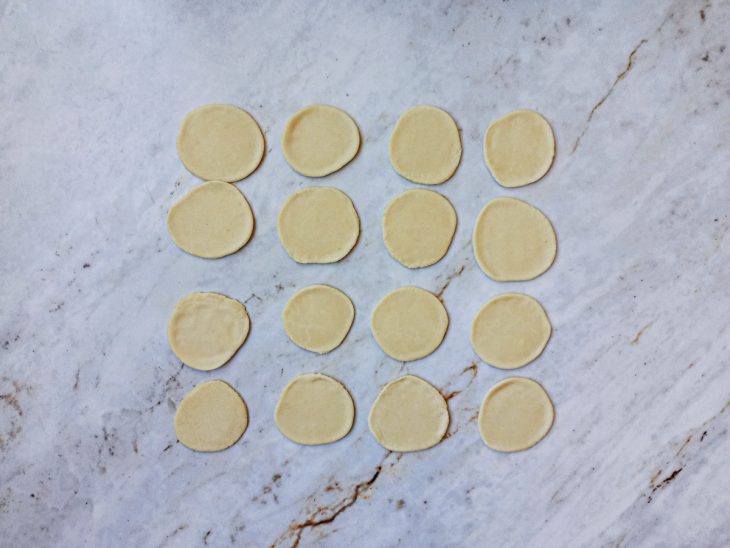 Na bancada, massa cortada em vários discos pequenos.