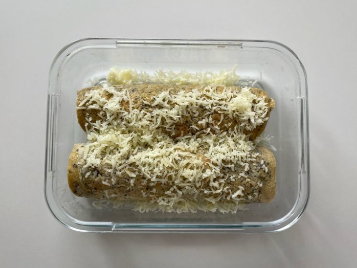 Panquecas recheadas acomodadas num refratário com queijo ralado por cima.