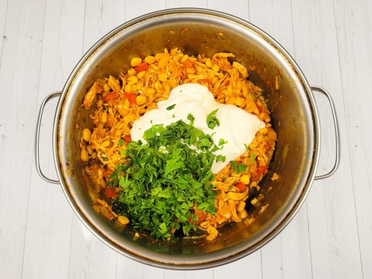 Uma panela refogando vegetais e frango desfiado temperado, com cheiro-verde e requeijão.