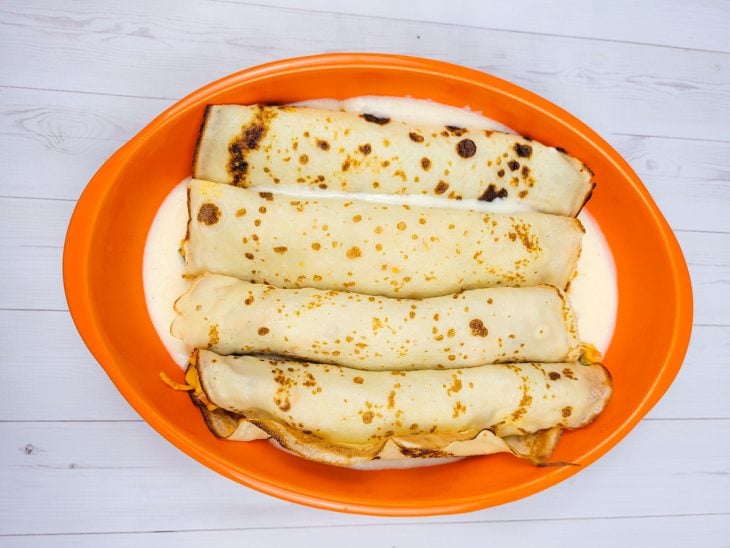 Uma travessa forrada com molho branco contendo panquecas de frango.