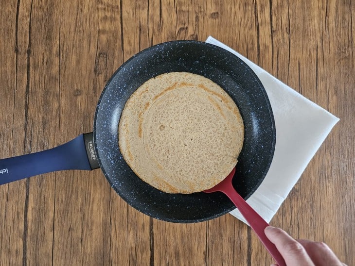 Espátula por baixo de uma panqueca na panela.