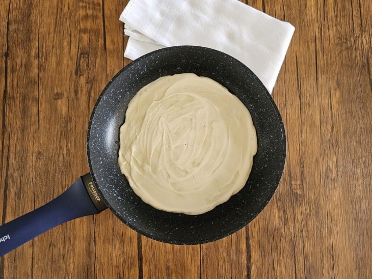 Frigideira com uma porção de panqueca bem espalhada.