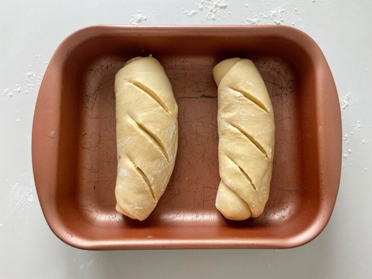 Pães modelados sendo acomodados em uma assadeira com espaço entre eles.
