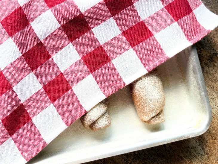 Rolinhos numa forma, cobertos com pano de prato.