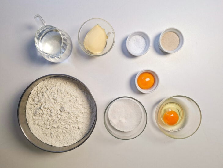 Ingredientes organizados na bancada com farinha, fermento, ovos e manteiga em potes.