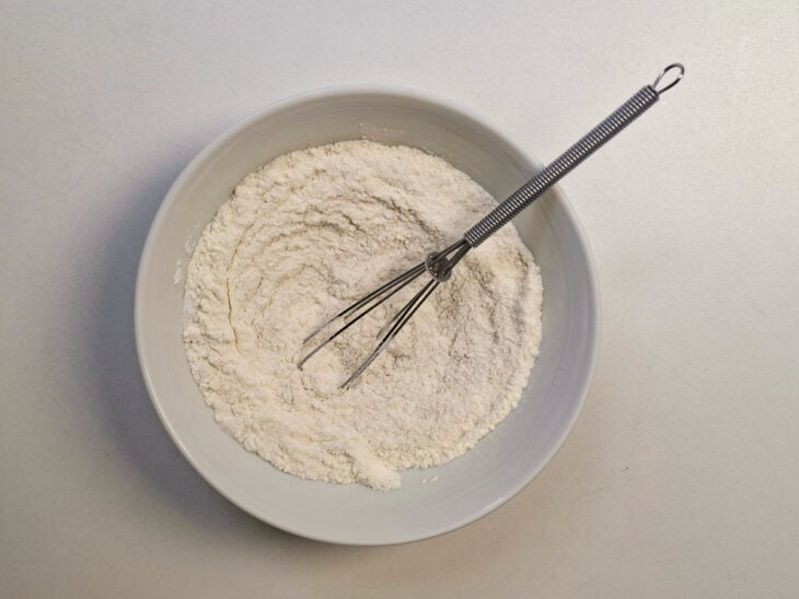 Farinha, fermento, açúcar e água misturados em uma tigela formando uma pasta.