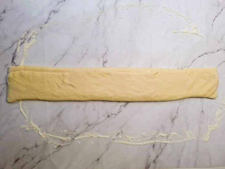 Outra lateral sendo sobreposta à primeira dobra para fechar o pão carteira.