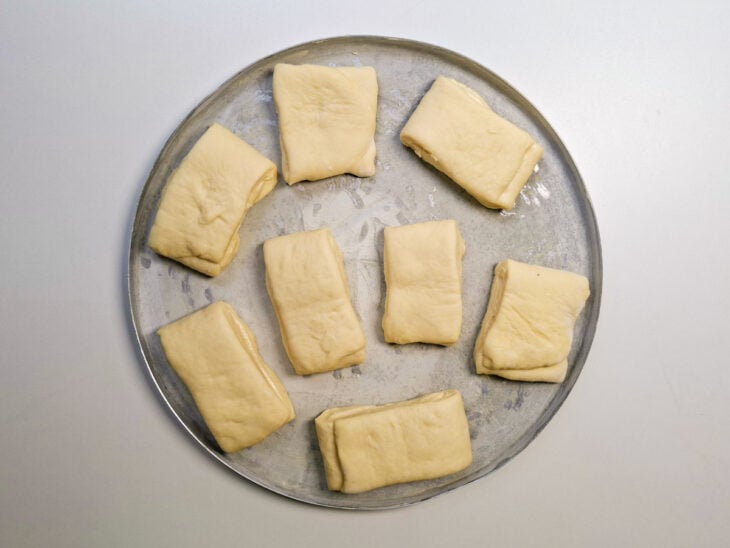Tiras de pão dispostas com espaço em uma assadeira untada.