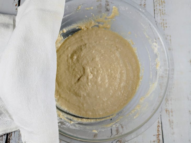 Massa de pão em uma tigela de vidro coberta com uma guardanapo de tecido.