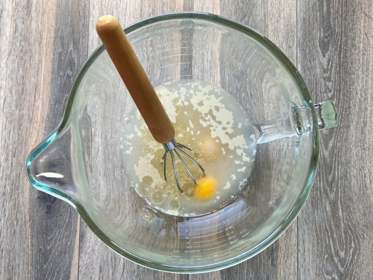 Um fouet e uma tigela com água, ovos, óleo, açúcar e fermento biológico.