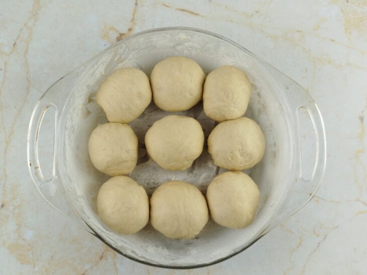 Nove bolinhas de massa modeladas e dispostas com espaçamento em uma assadeira de pizza untada.