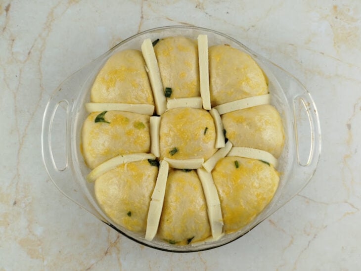 Tiras de queijo mussarela sendo encaixadas dentro dos cortes na massa do pão.