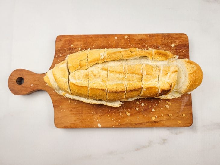 Uma tábua contendo um pão italiano recheado e com cortes.