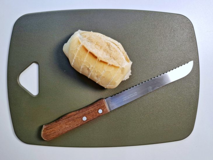 Pão francês com cortes verticais sobre uma tábua de cozinha.