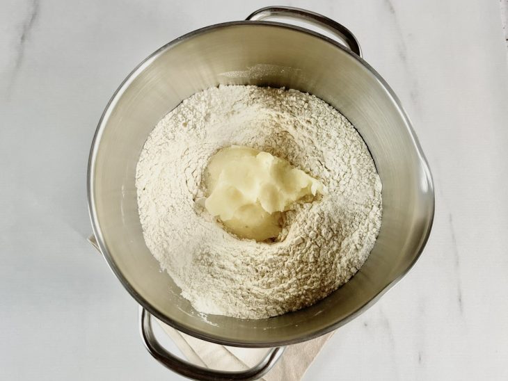 Farinha, sal, fermento, açúcar, batatas cozidas e amassadas, ovo inteiro e azeite na tigela da batedeira.
