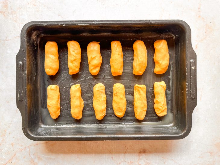 Pãezinhos acomodados em assadeira untada e enfarinhada.