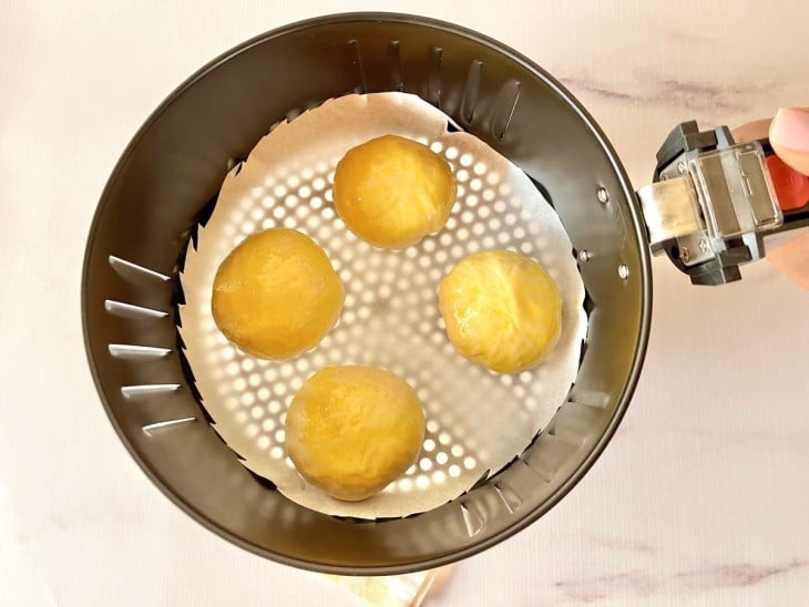 Uma cesta de airfryer contendo quatro massinhas de pães de batata recheados.