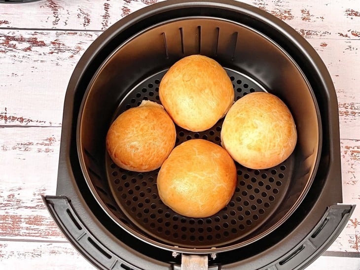 Uma cesta de airfryer contendo quatro pães de batata recheados.
