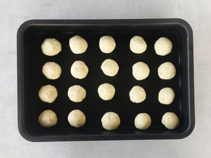 Bolinhas modeladas e distribuídas em uma assadeira com espaço entre elas.