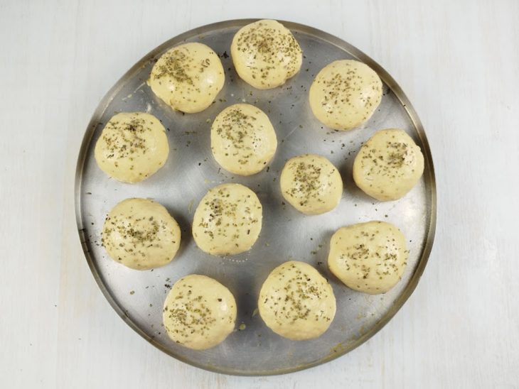 Orégano salpicado sobre as bolinhas de pão.