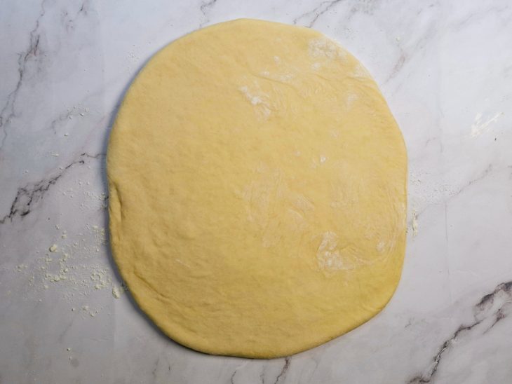 Massa aberta com rolo sobre superfície enfarinhada.